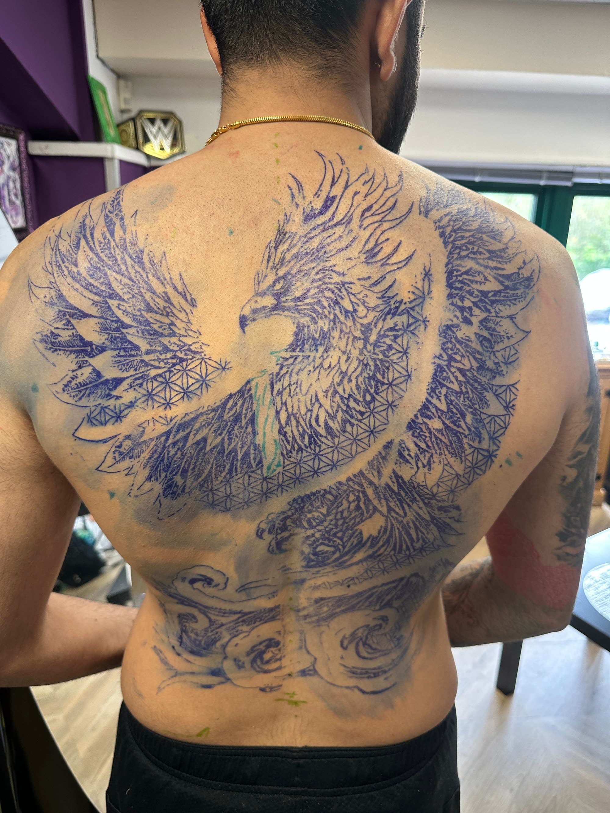 The phoenix back piece as a purple stencil on skin, before the first line