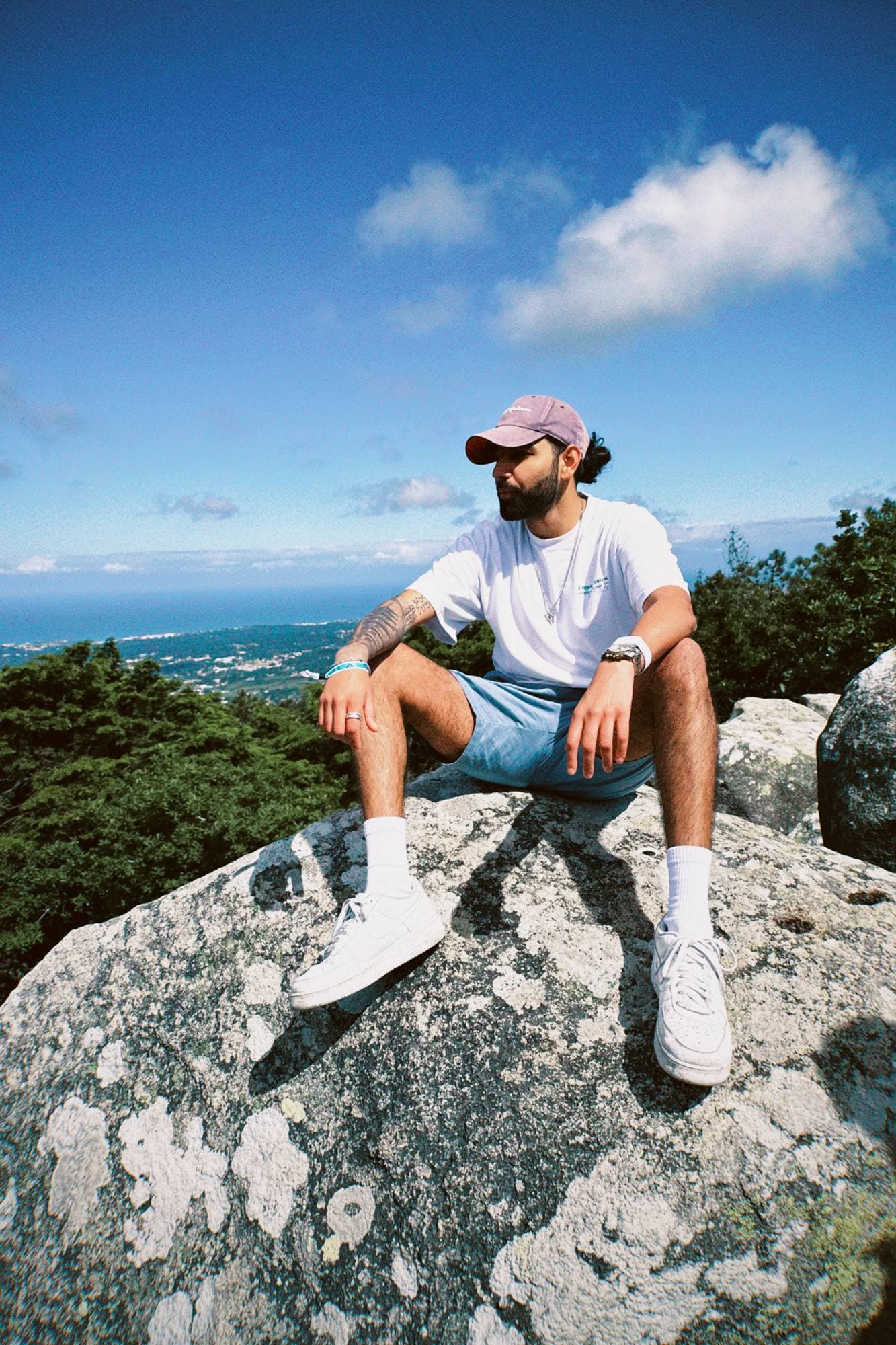 Param sitting on a lichen-covered boulder above a forest, the sea on the horizon