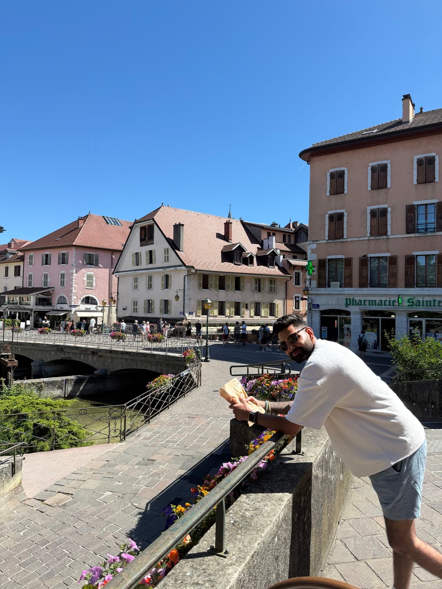 Me in sunglasses and a white T-shirt leaning on a bridge rail over the canal, a paper bag of pastries in my hand
