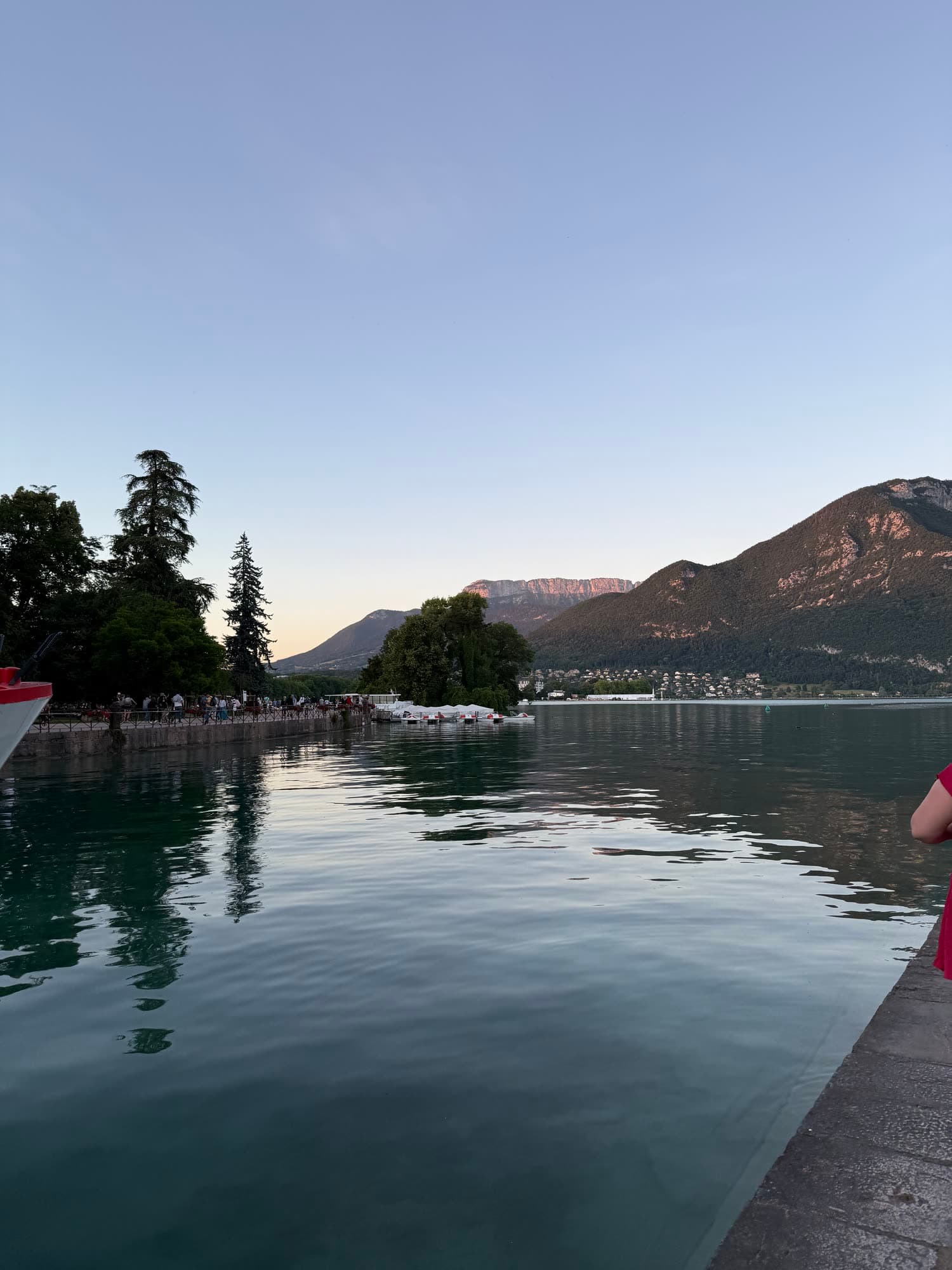 Lake Annecy after sunset, still water reflecting trees and the mountains across the lake