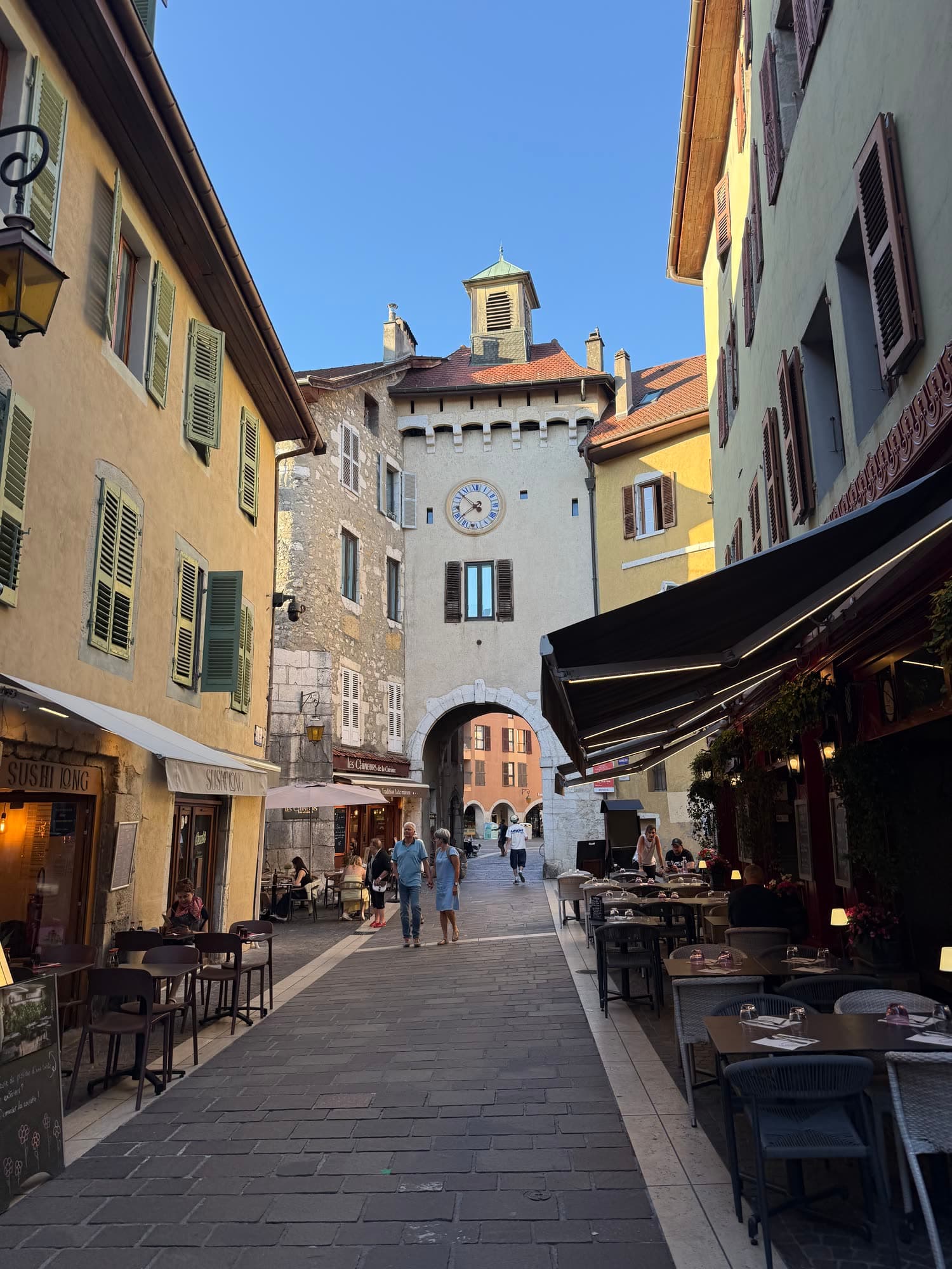 A narrow street of painted houses and café terraces in old Annecy, a gate tower at the far end