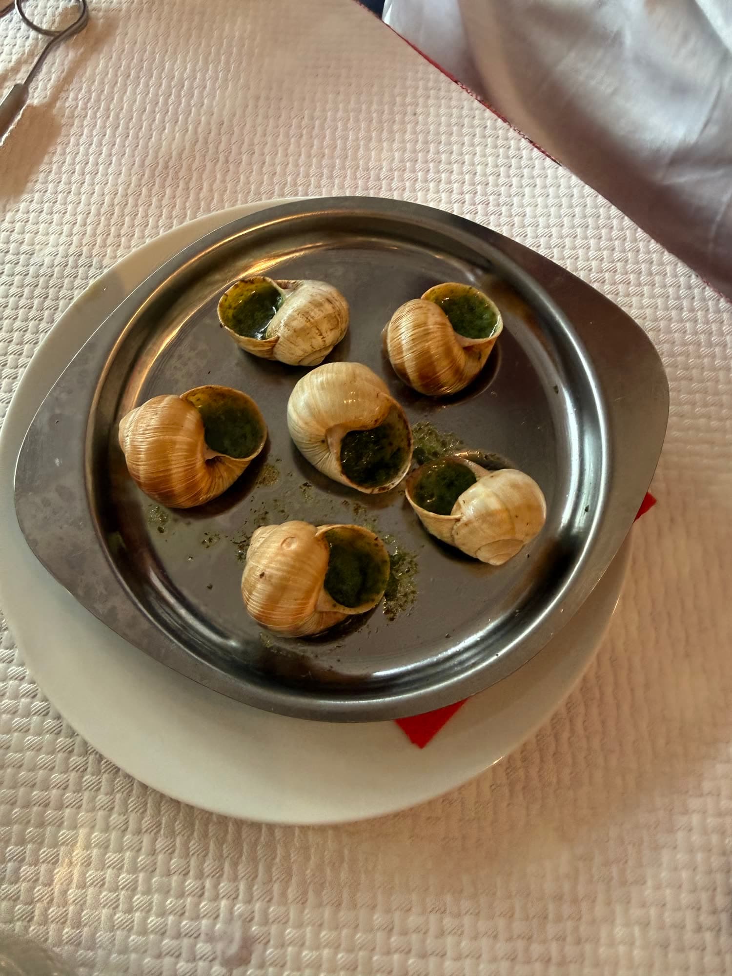 Six snails in garlic and parsley butter on a metal escargot plate
