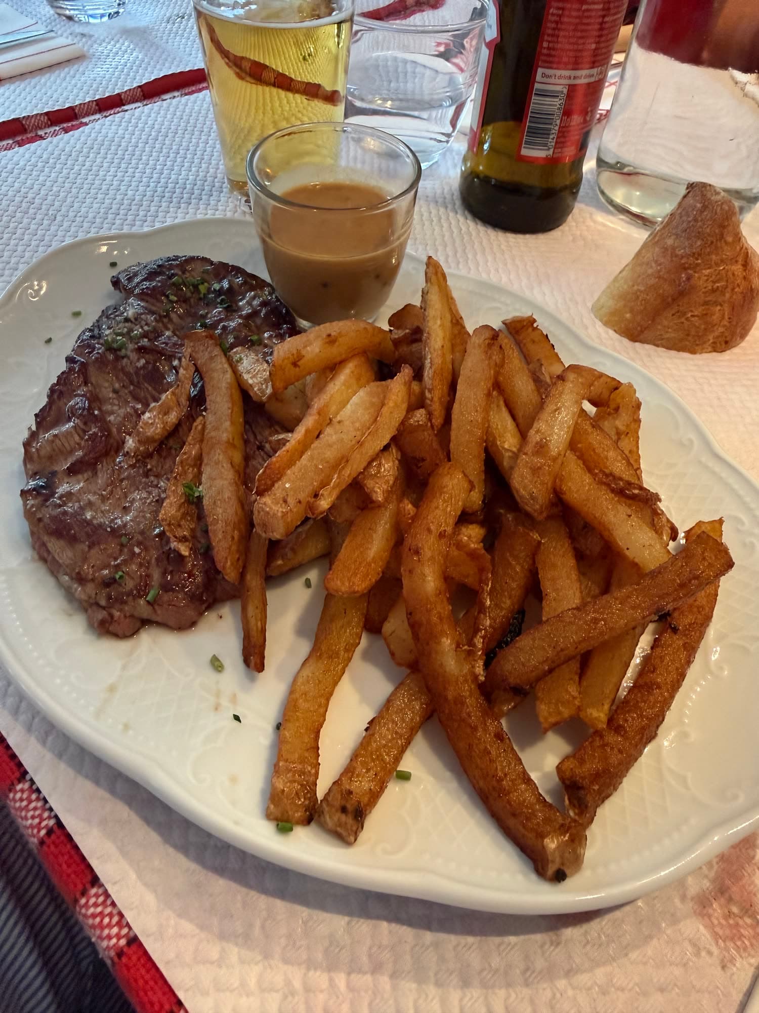 A plate of steak and a heap of chips with a small pot of sauce
