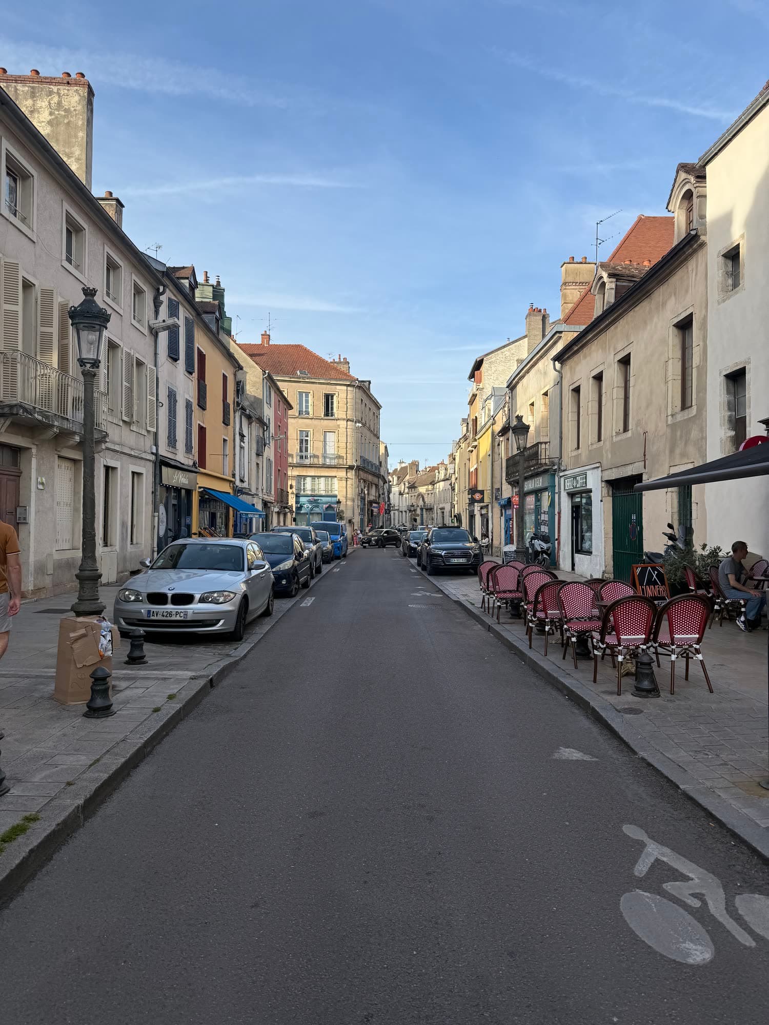 A Dijon street of stone houses in evening light, café chairs set out along the pavement