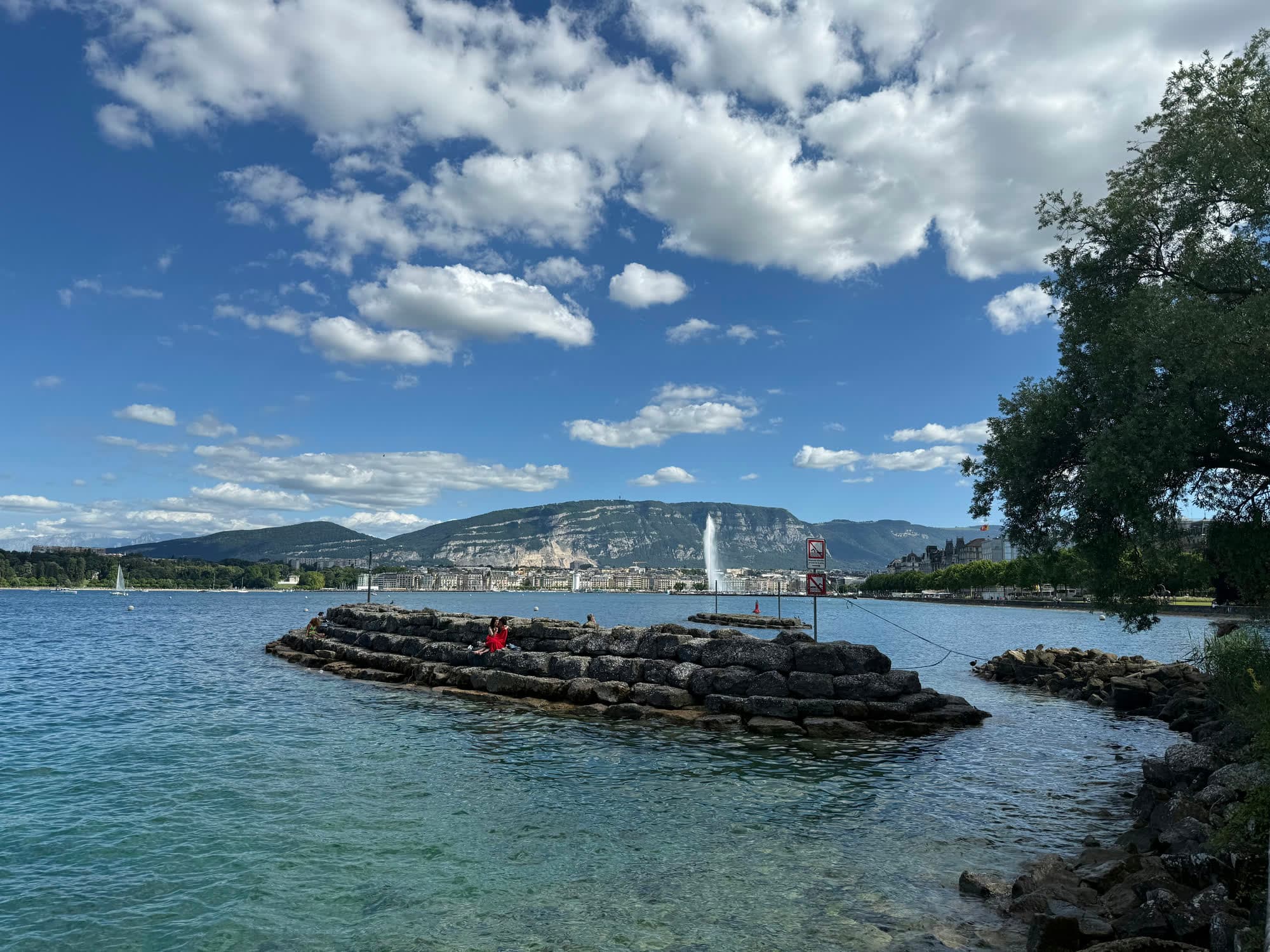 A stone breakwater in turquoise water, the Jet d’Eau rising from the far side of the bay