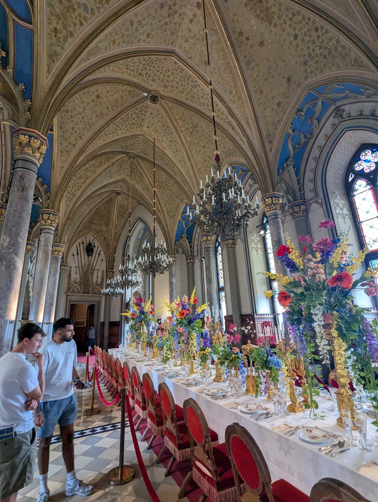 Two of us beside a long banqueting table set with flowers under a painted Gothic vault
