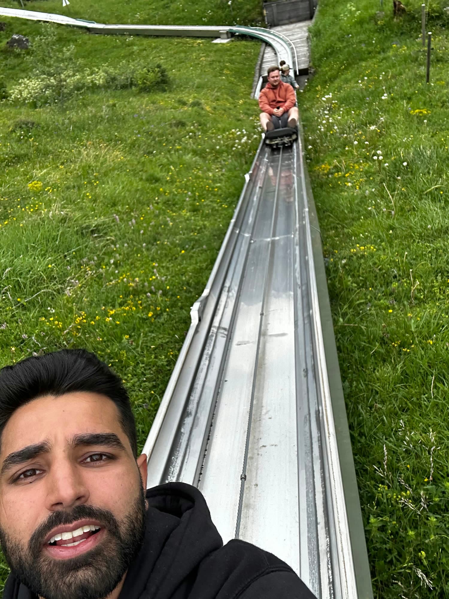 Selfie of me mid-sentence, the toboggan rail running straight down the hill behind