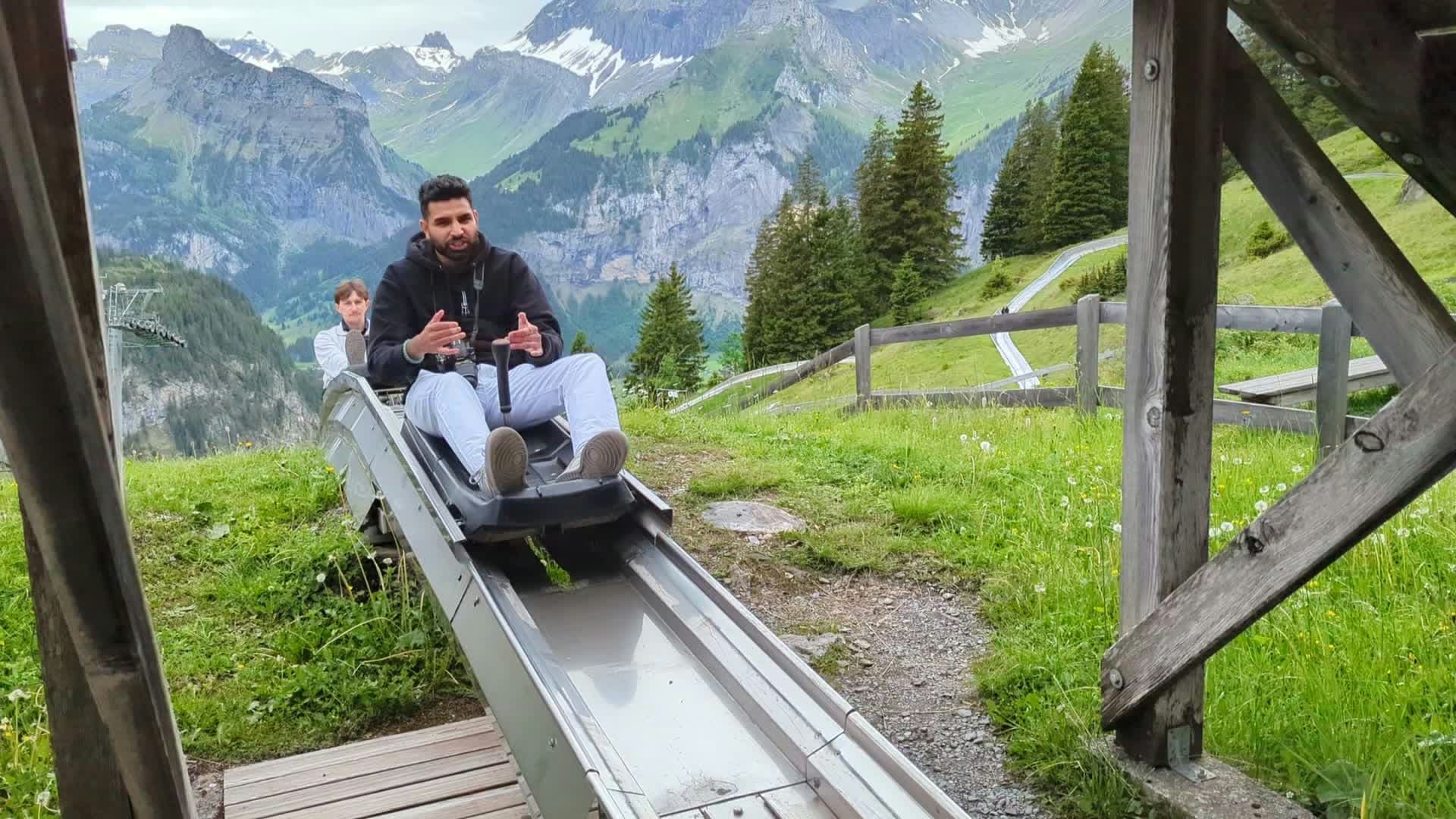 Me riding a toboggan sled out of a wooden shelter onto the rail, mountains behind