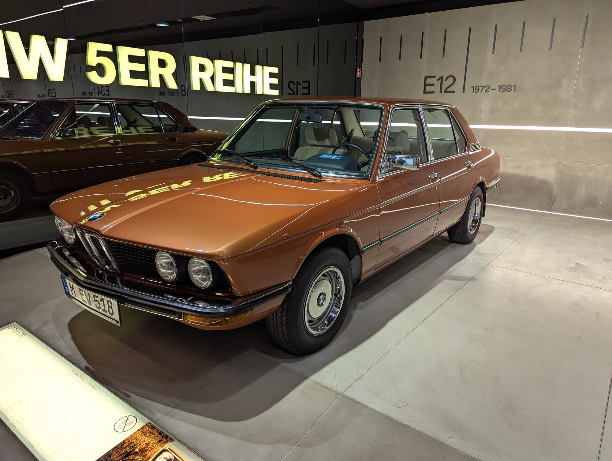 A bronze BMW E12 5 Series at the head of a row of later 5 Series under a lit BMW 5ER REIHE sign