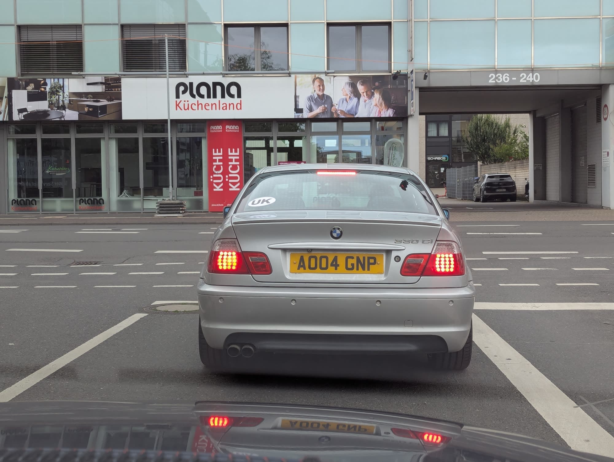 The silver BMW coupe from behind at a town junction, its brake lights on
