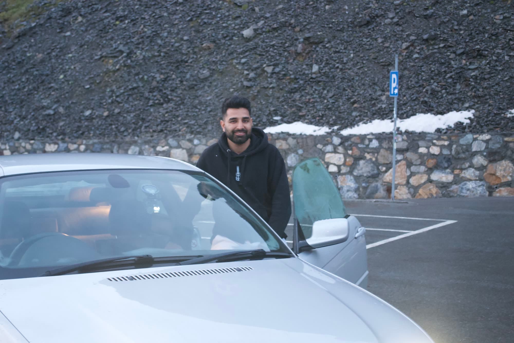 Me standing behind the open door of the silver BMW coupe in the summit car park, scree and snow behind