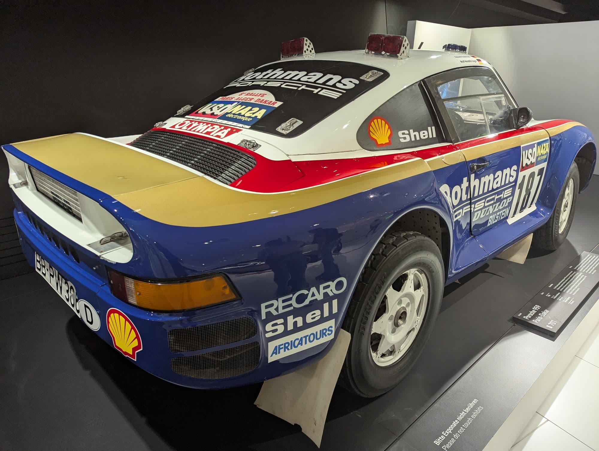 Rear three-quarter view of a Porsche 959 in blue and white Rothmans rally livery