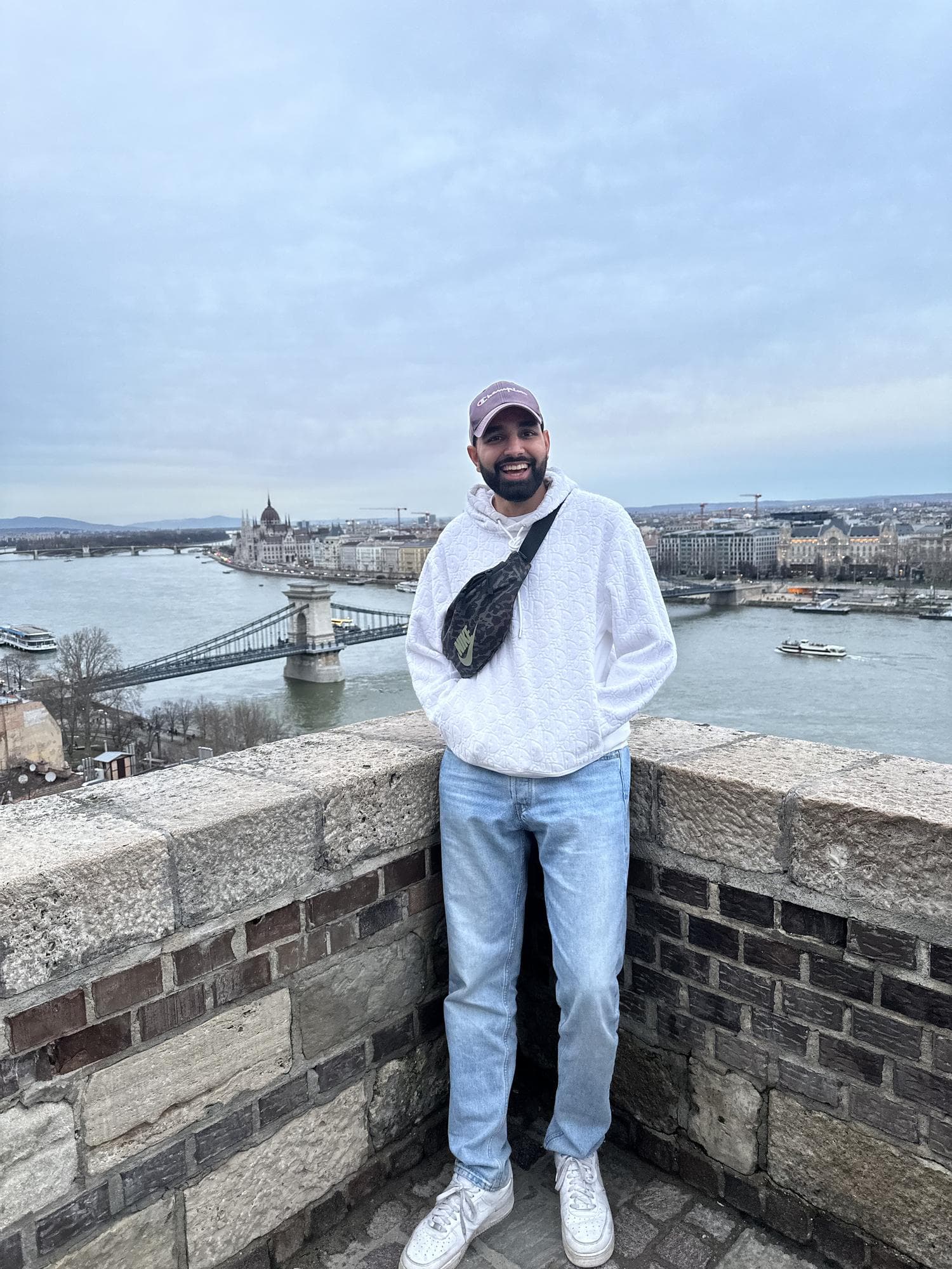 Param leaning on a stone parapet on Castle Hill, the Chain Bridge and the Parliament building on the river below