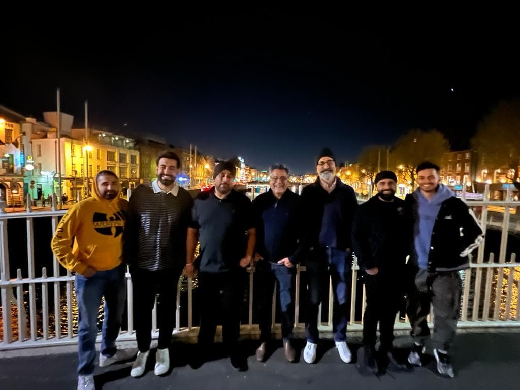 Seven men in a row on a bridge at night, me on the far left in a yellow hoodie, lit quayside buildings behind
