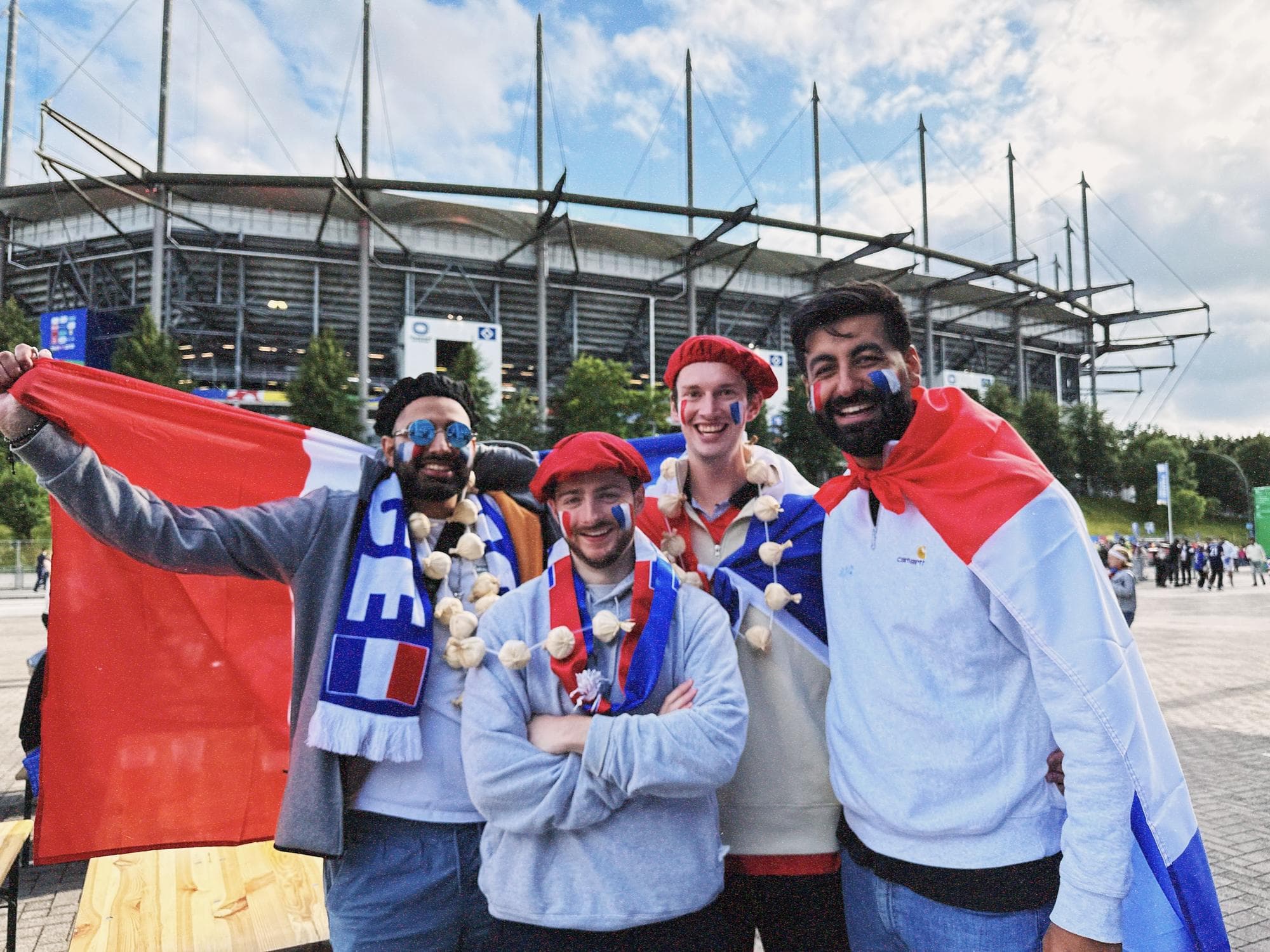 Param holding up a French flag with three friends in berets and garlic necklaces in front of the Volksparkstadion