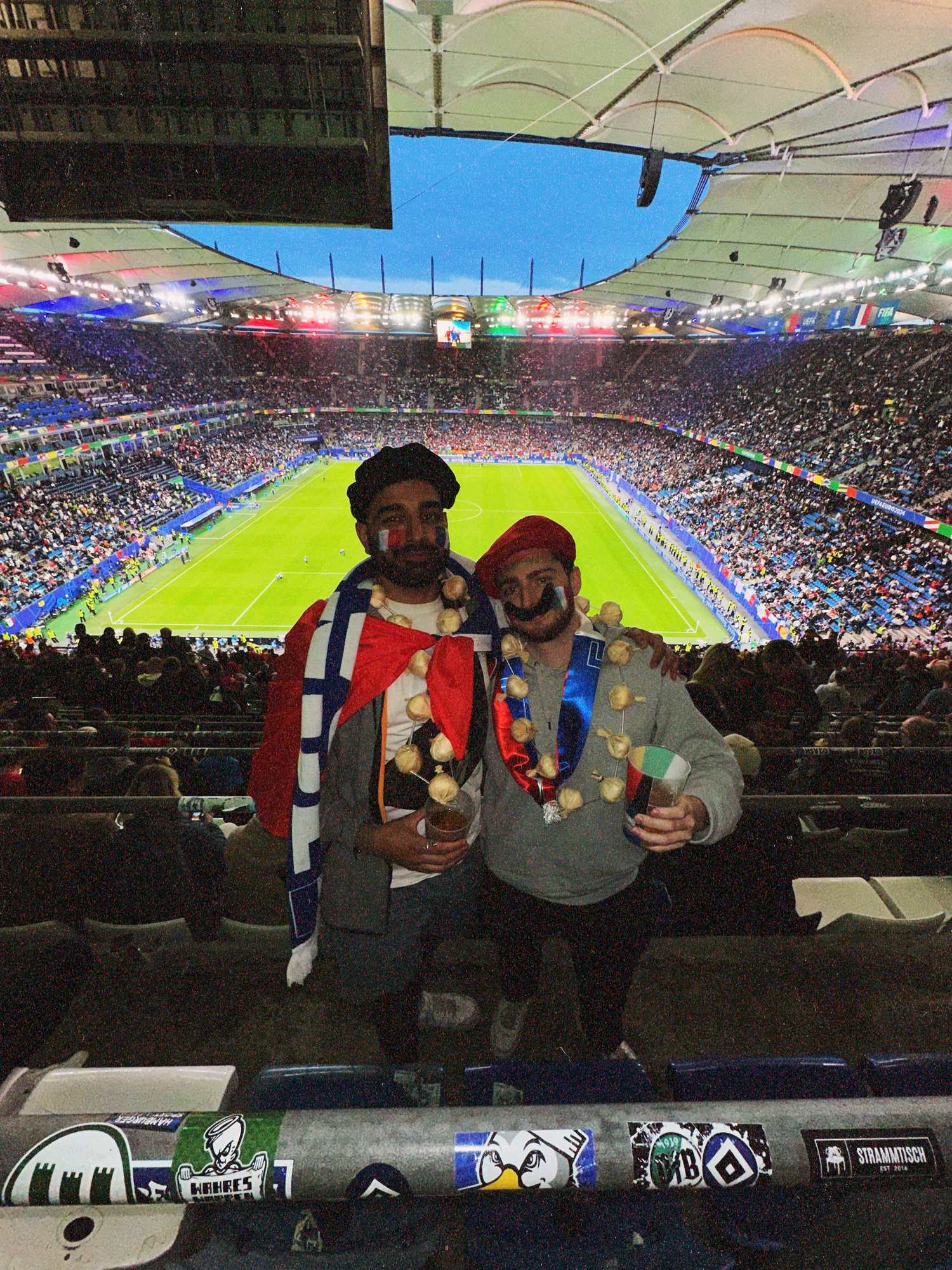 Param and a friend in berets and garlic necklaces standing in the upper stand, the floodlit pitch and crowd far below