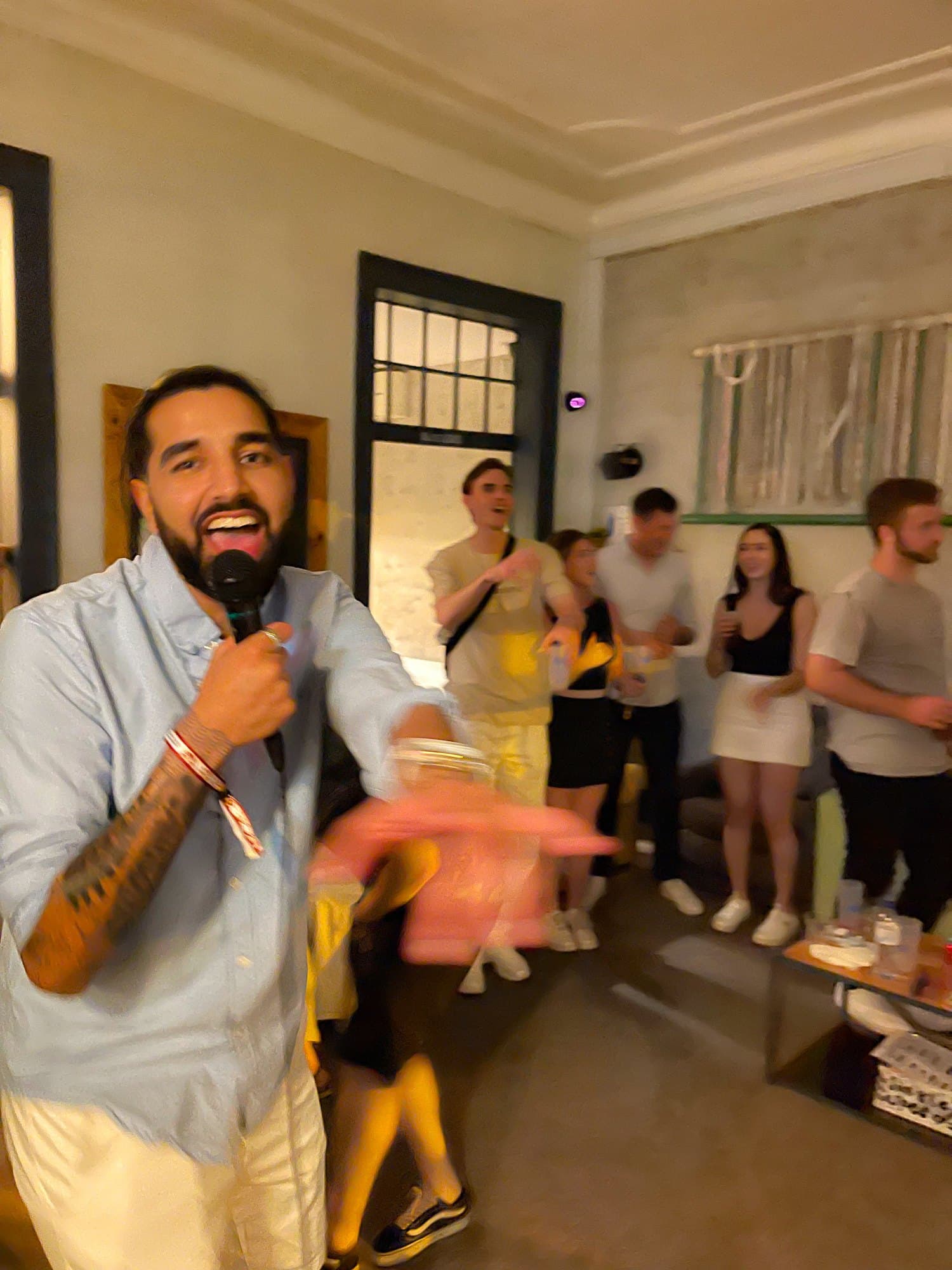 Param laughing into a microphone at a karaoke night, a room of people behind him