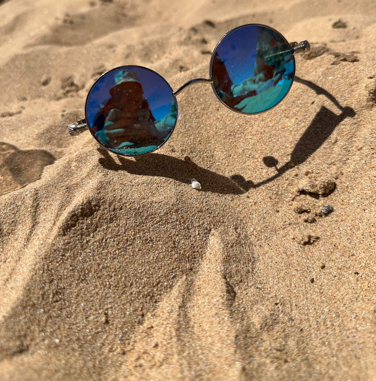 Round mirrored sunglasses resting in the sand, casting a long shadow