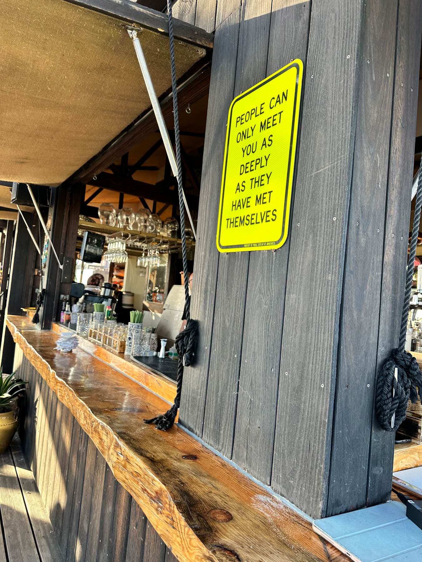 A yellow sign on a beach-bar post reading: people can only meet you as deeply as they have met themselves
