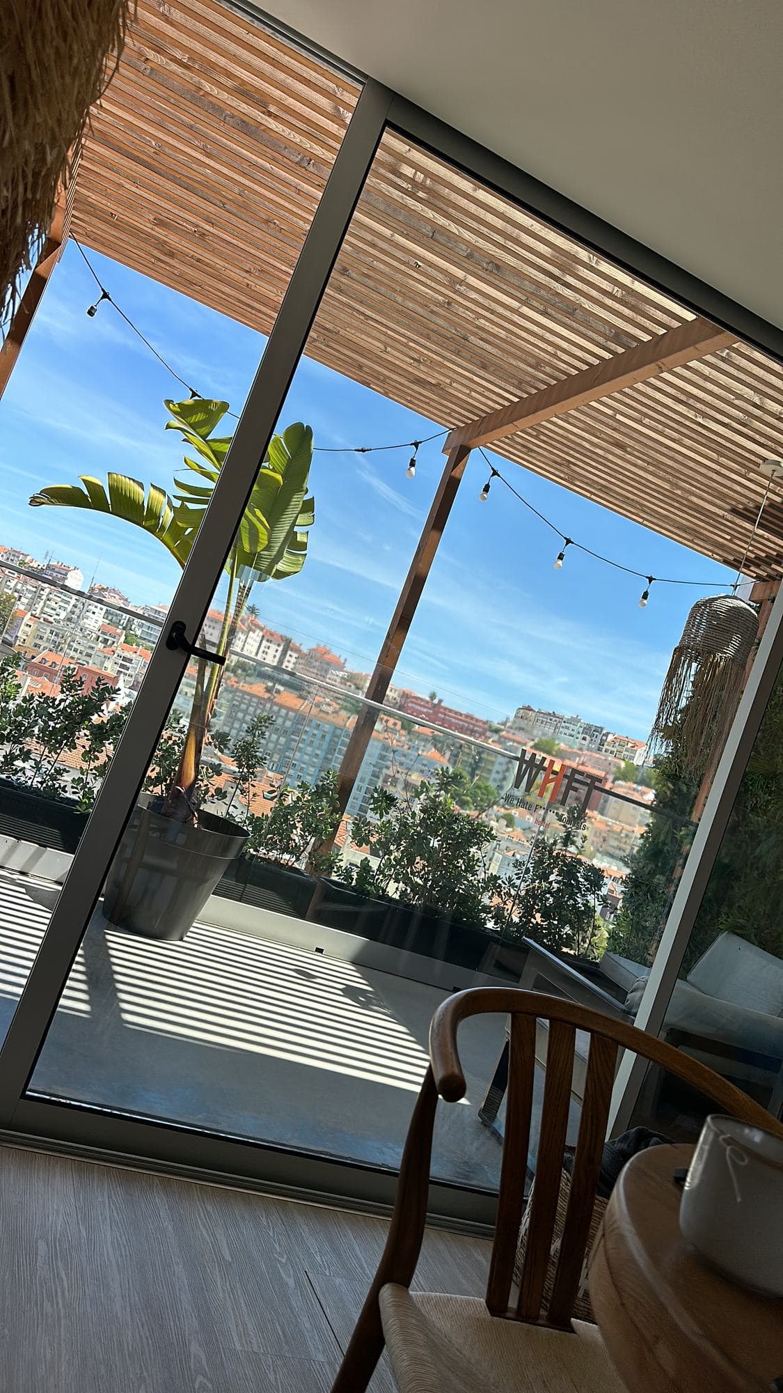 A terrace under a slatted wooden roof, a plant and string lights framing a view over Lisbon rooftops
