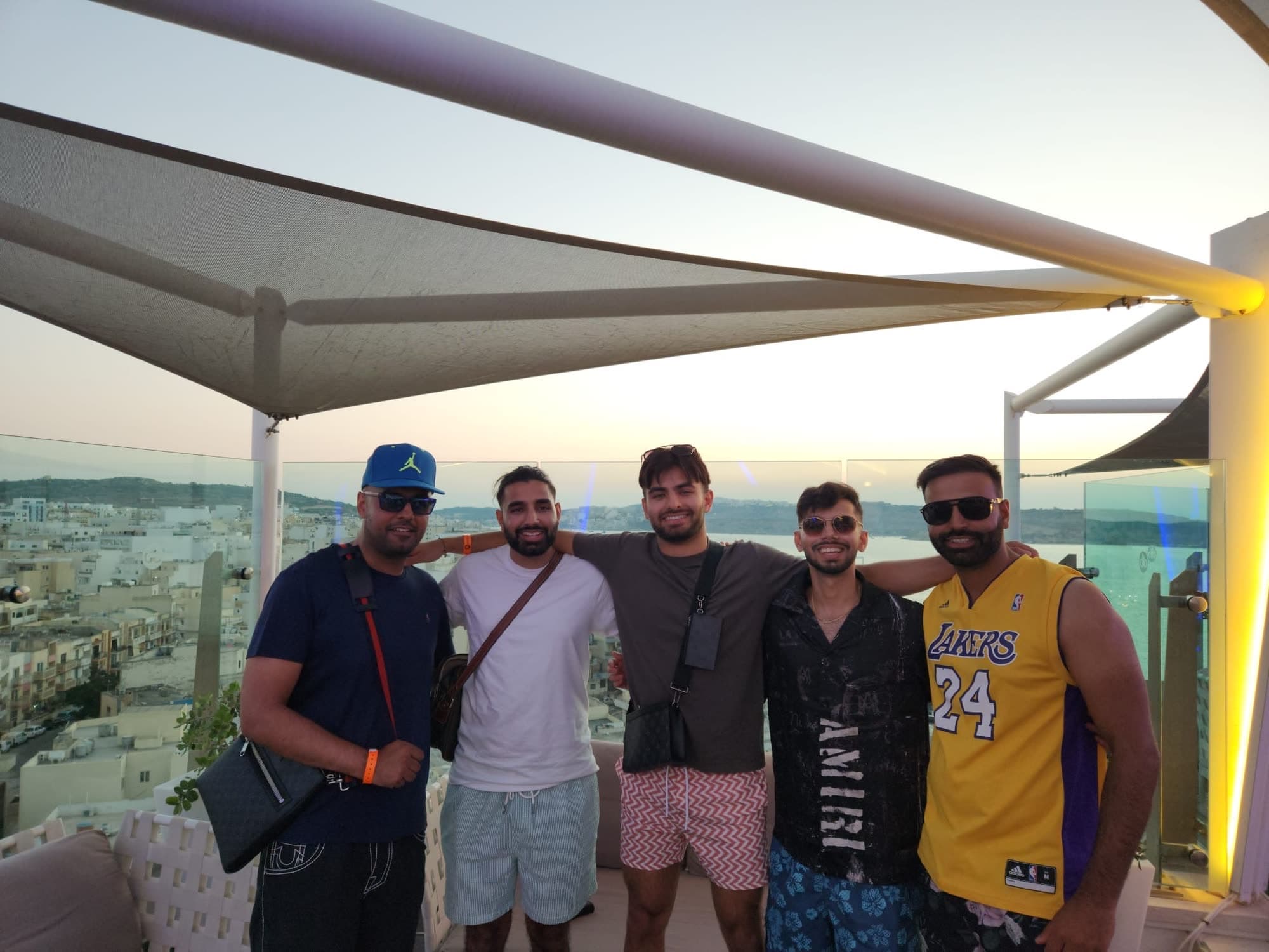 The same five men under a white sail canopy on a rooftop bar, me second from the left, the town and the sea behind