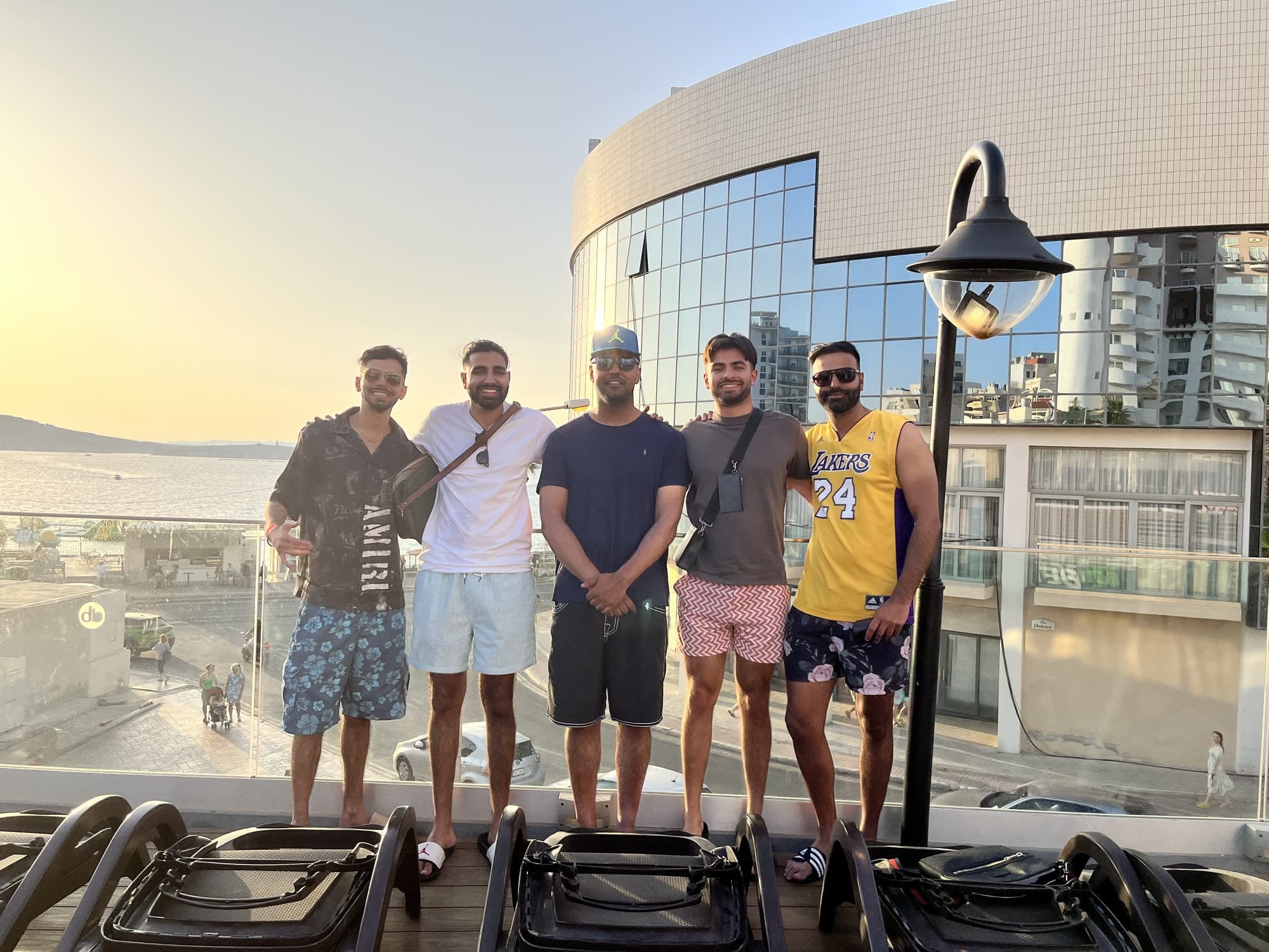 Five men standing in a line on a hotel terrace at sunset, me second from the left in a white T-shirt, a curved glass building behind