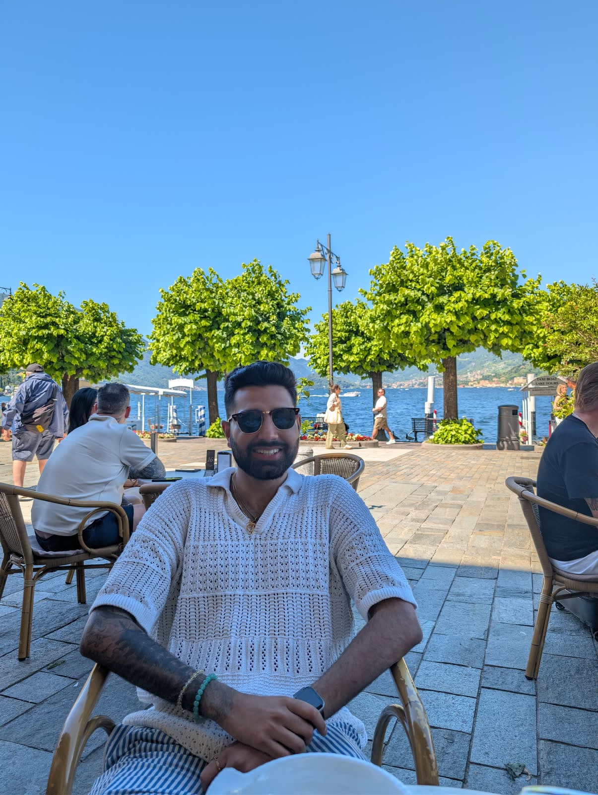 Me in sunglasses at a café table on a Bellagio square, the lake and plane trees behind