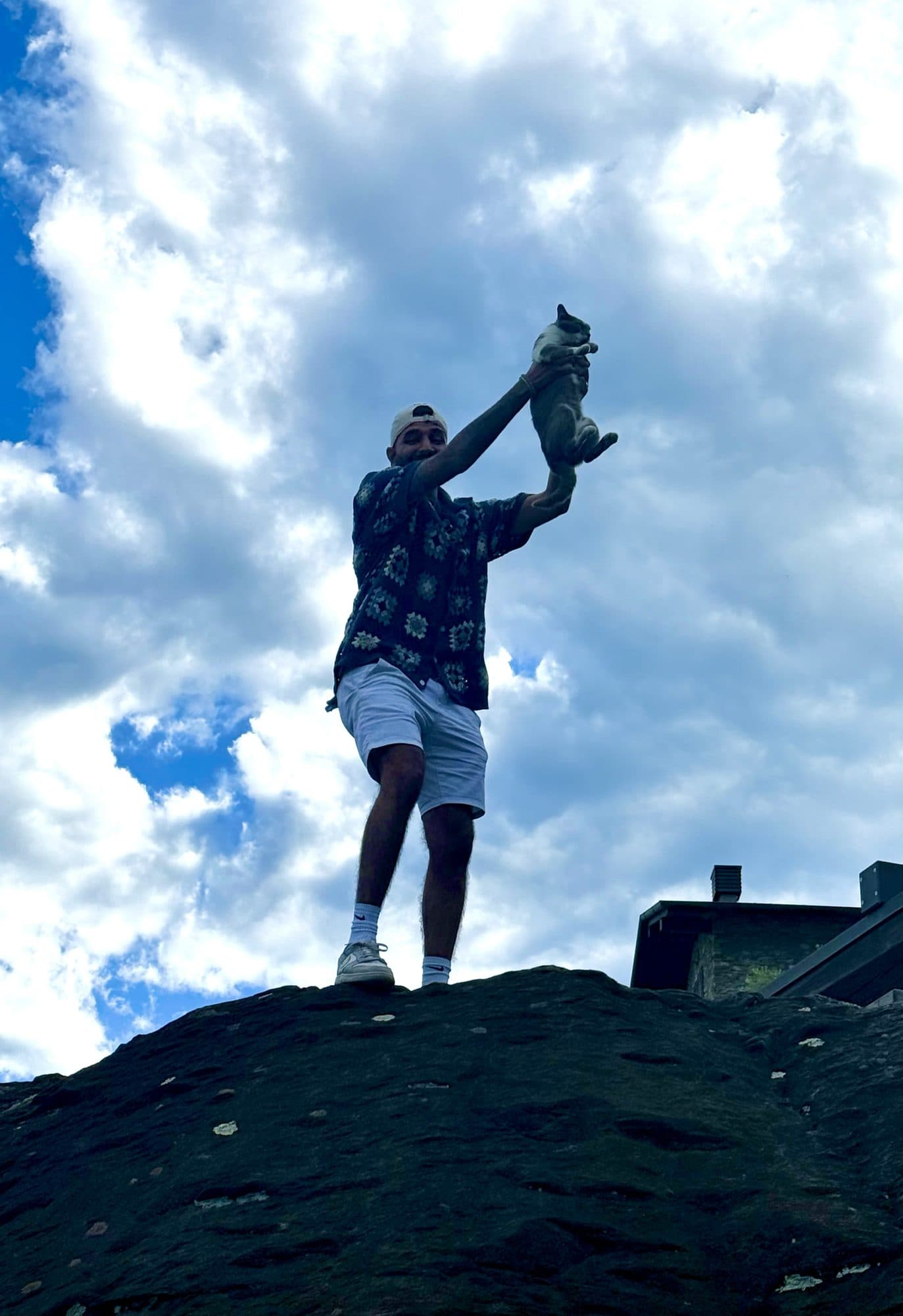 Me standing on a rock against a cloudy sky, holding the grey and white cat up above my head