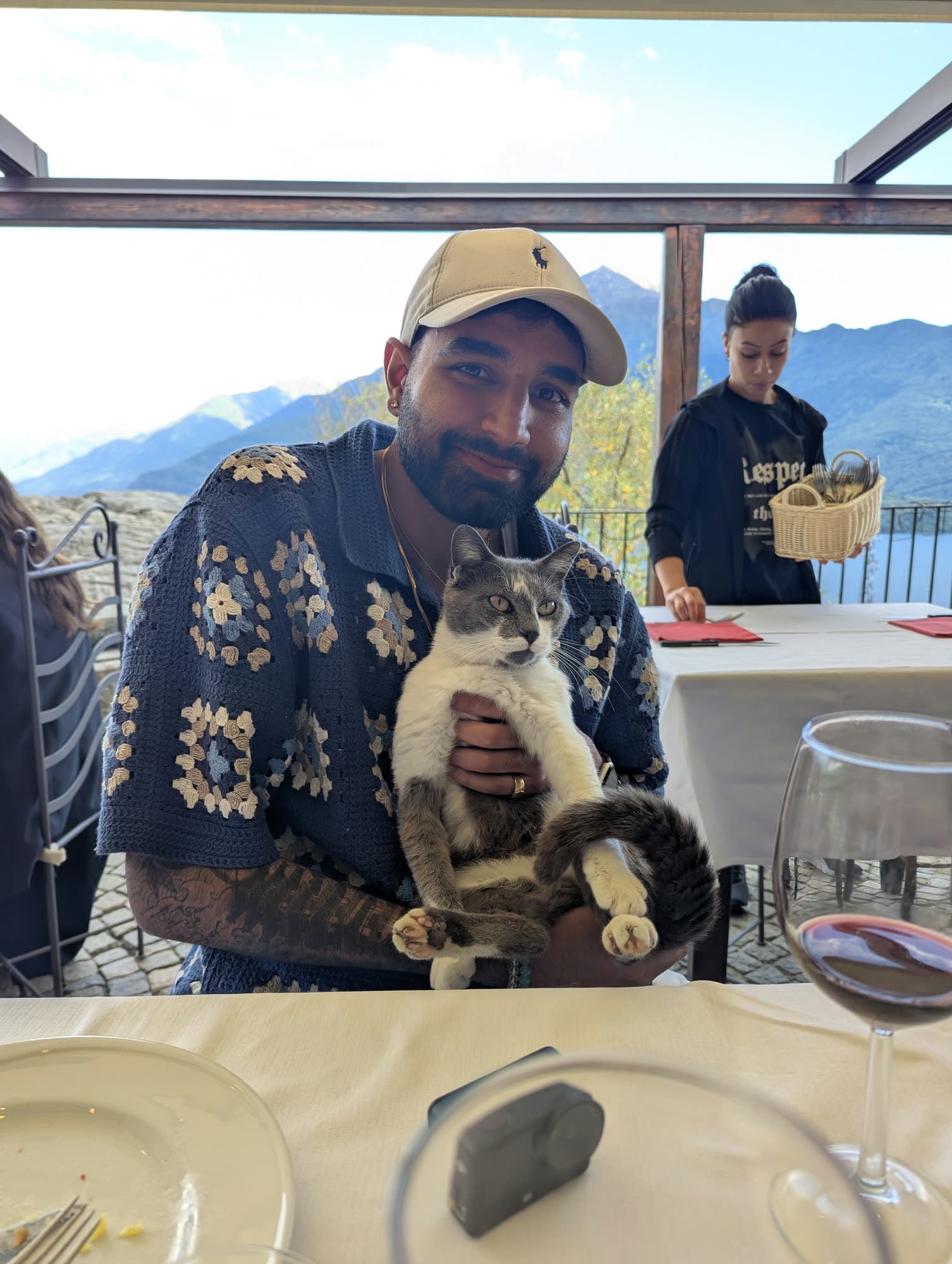 Me holding a grey and white cat at a restaurant table, the lake behind