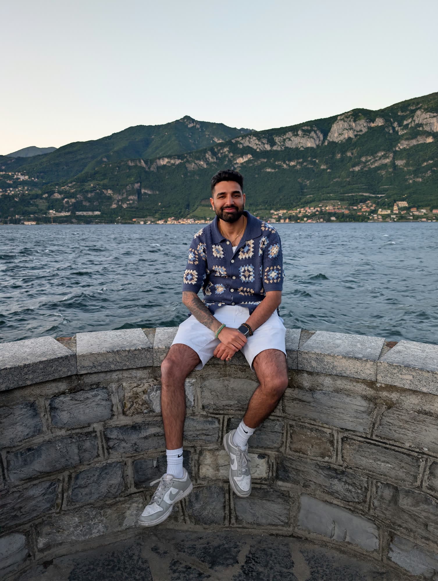 Me seated on a curved stone wall above the lake at dusk