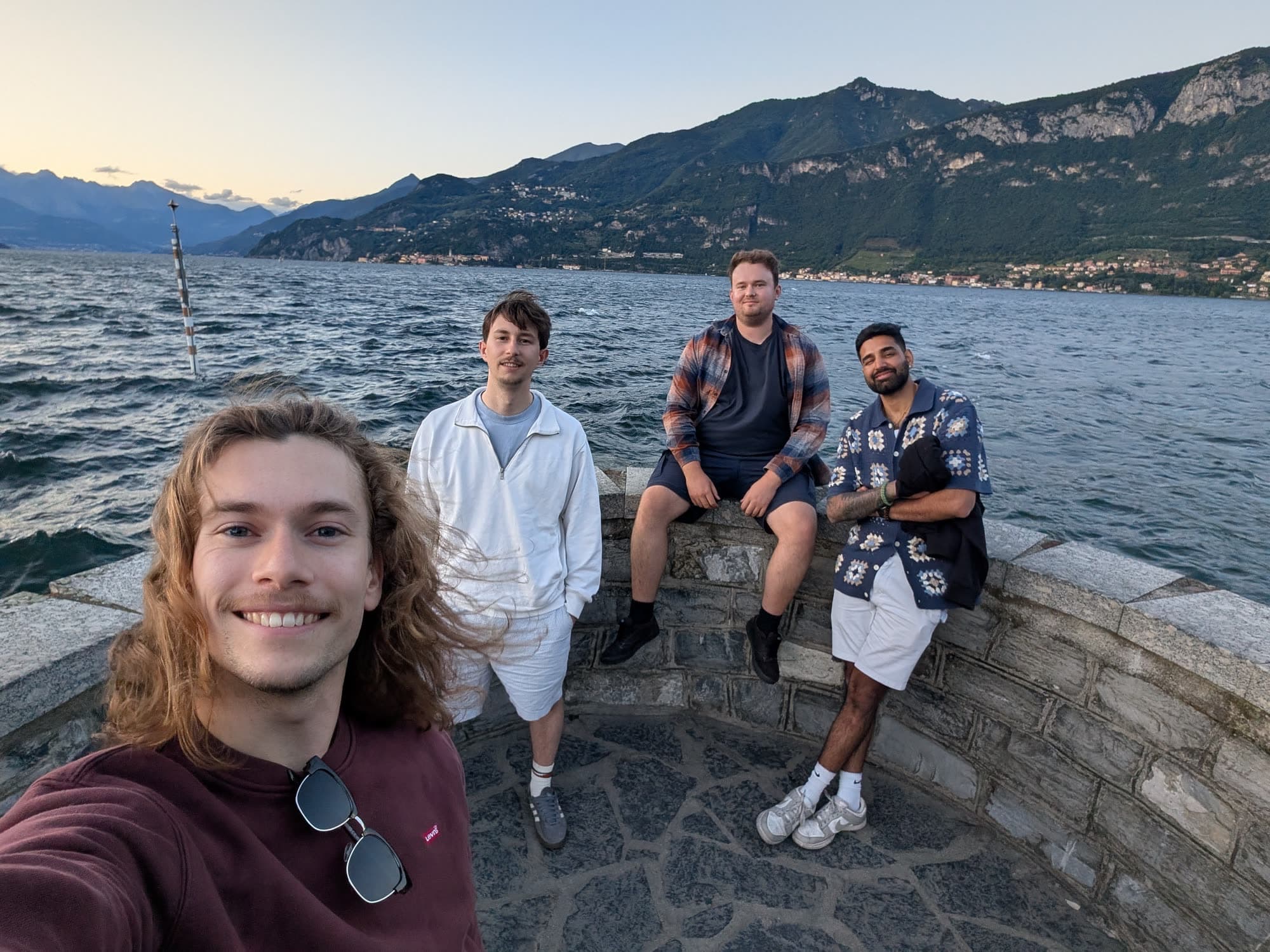 Selfie on the lake wall at Lake Como: a friend in front, me and two friends on the stone wall behind, mountains across the water