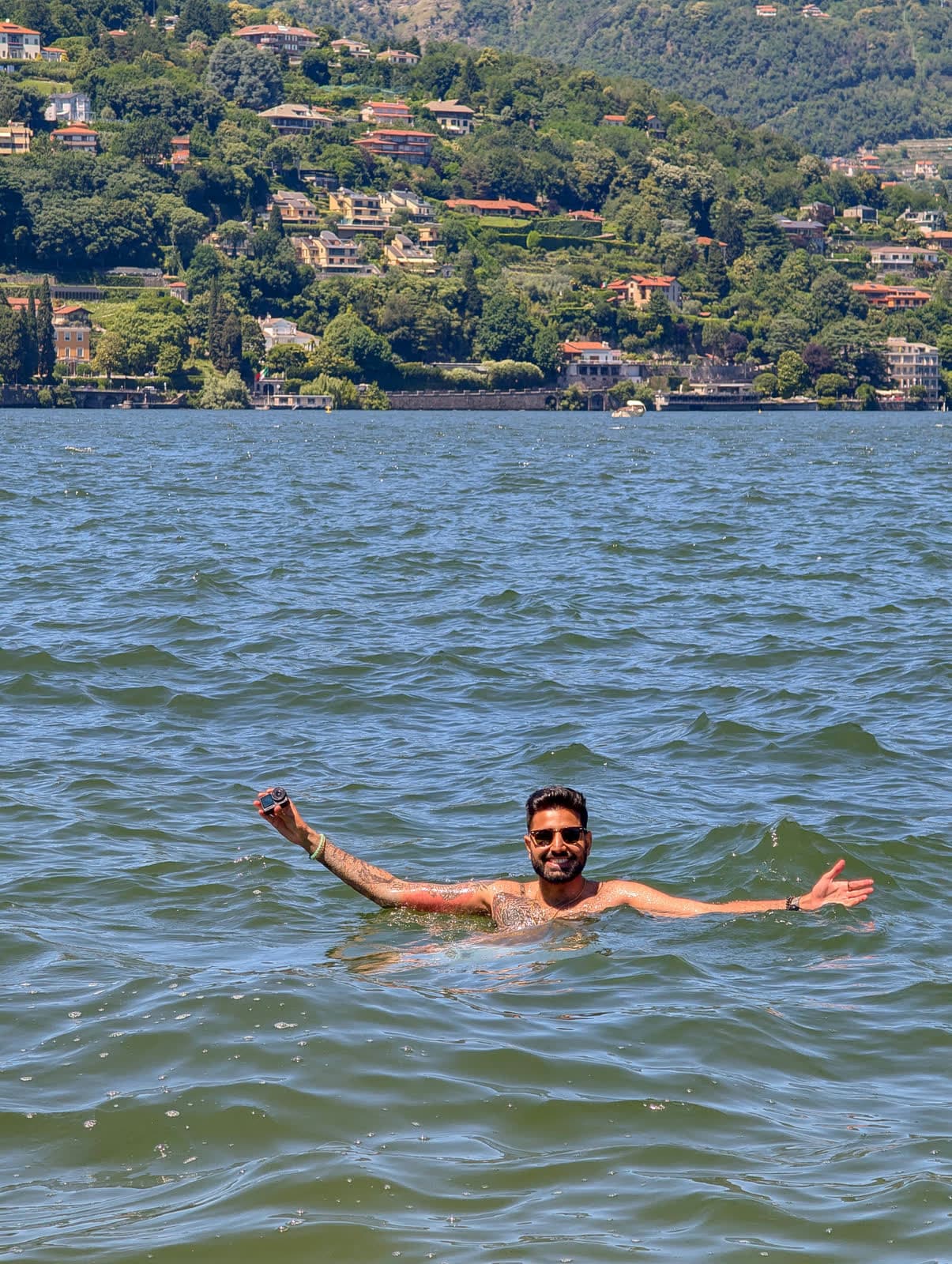 Me swimming in the lake with my arms spread, villas on the hillside behind
