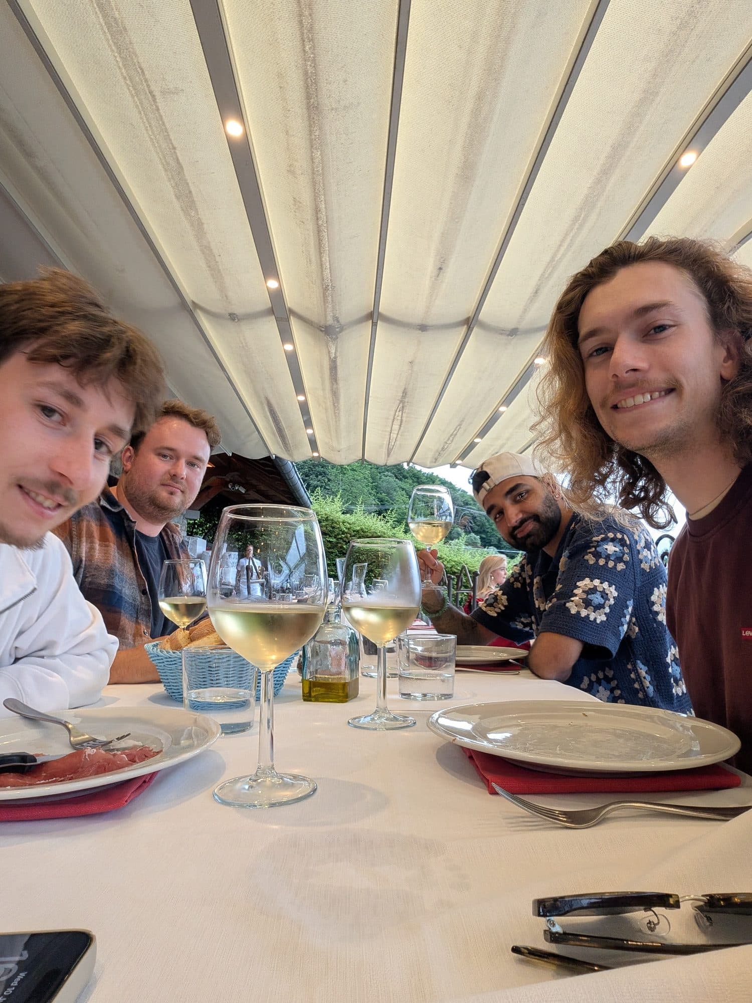 The four of us at a long white table under an awning, glasses of white wine in front of us