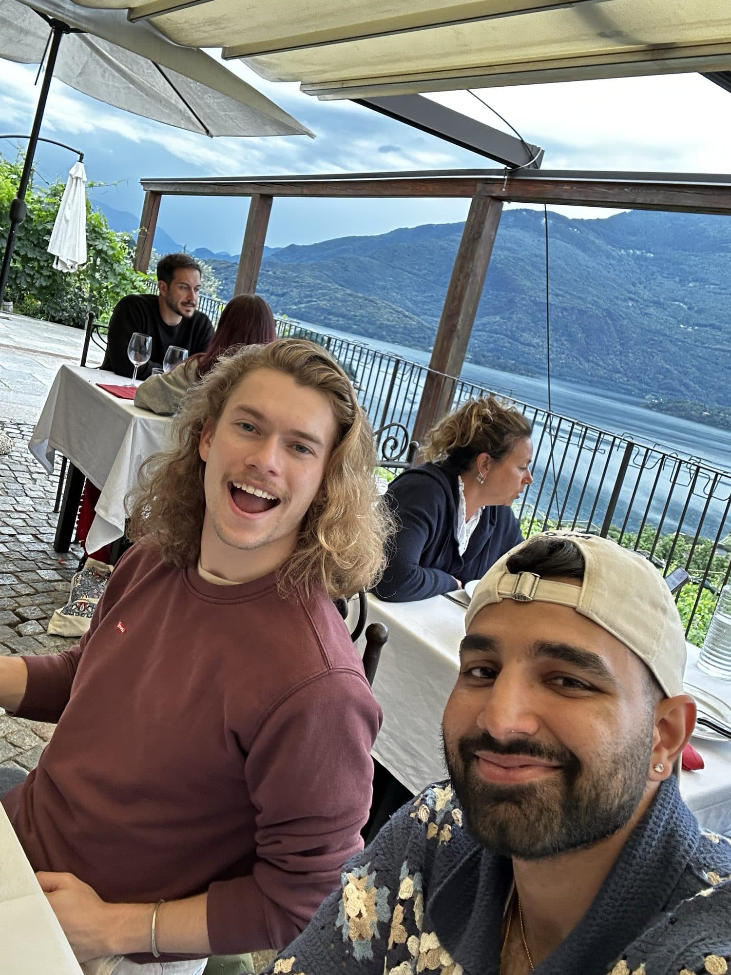 Selfie of me in a cap with a friend laughing beside me, on a winery terrace above the lake