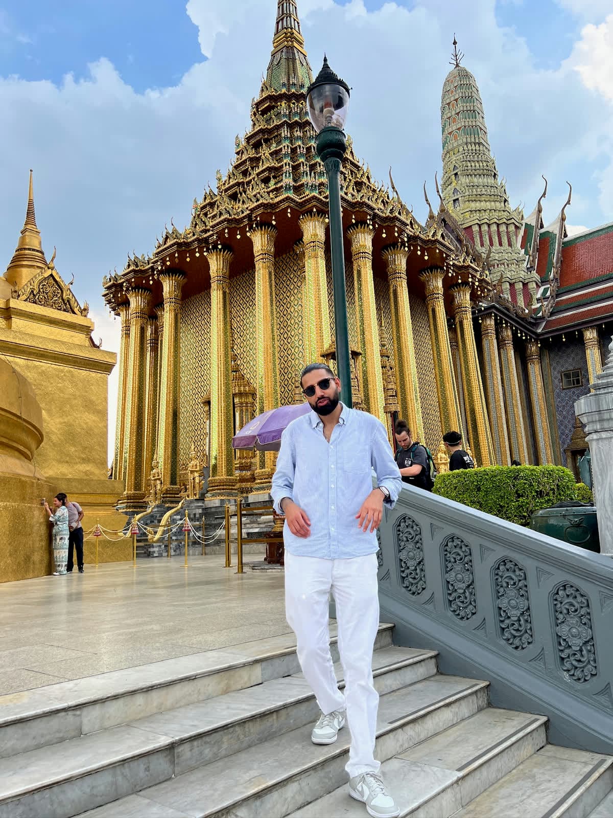 Param in sunglasses walking down marble steps in front of a gilded temple hall with tall golden columns
