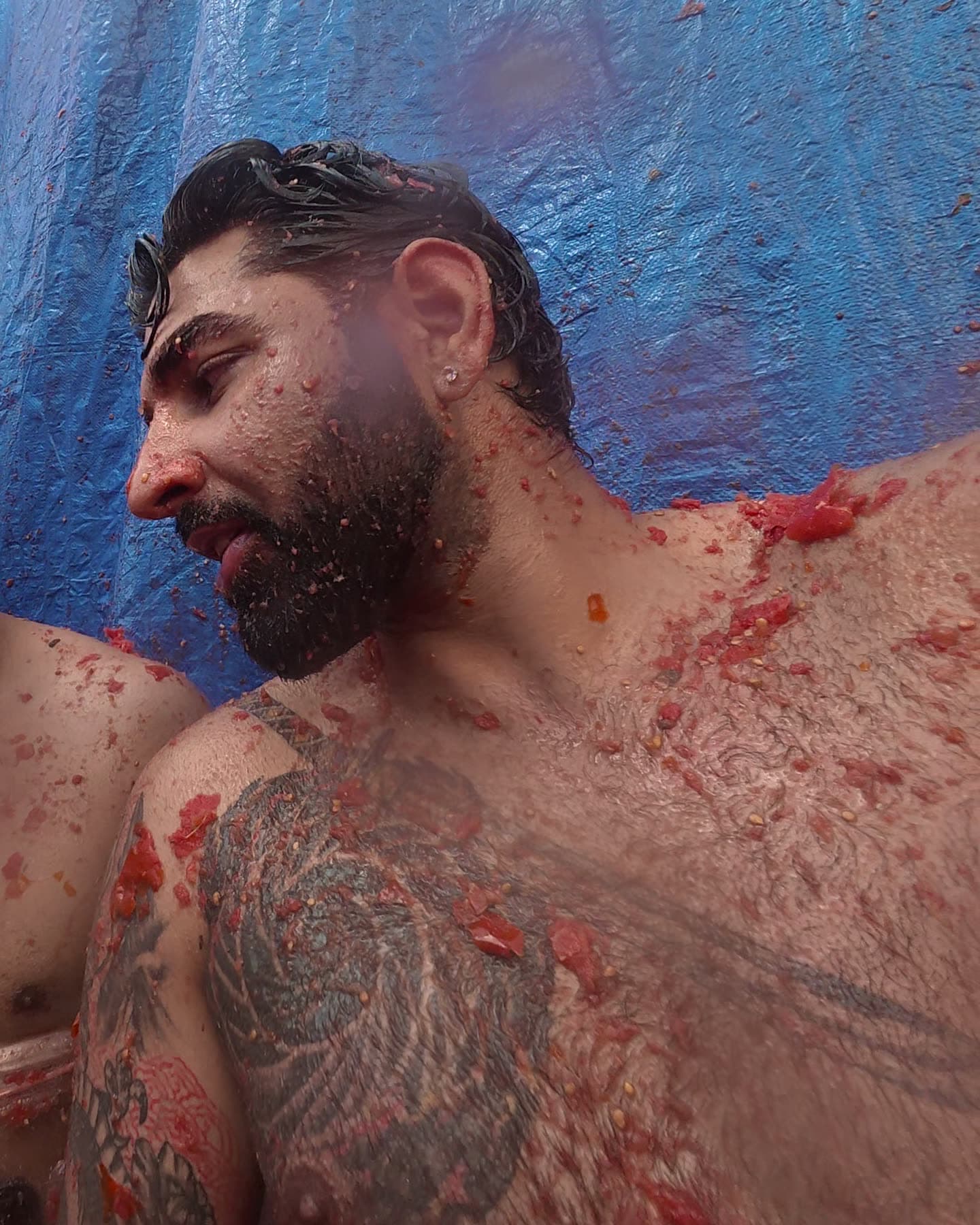 Me shirtless against a blue tarp, chest tattoo and beard spattered with tomato