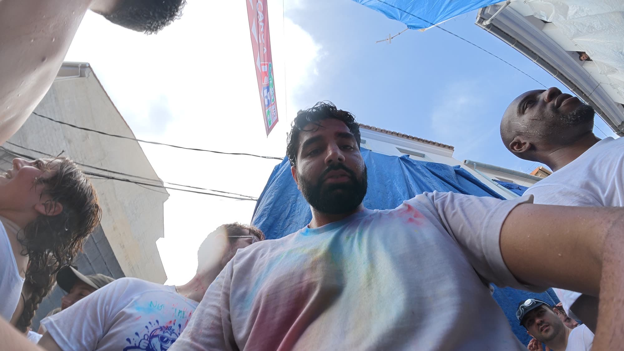 Me from below in a powder-stained white shirt, blue tarps and a festival banner overhead