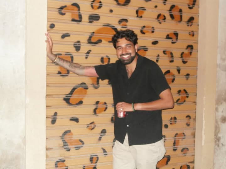 Me in a black shirt leaning on a roller shutter painted in leopard print, at night