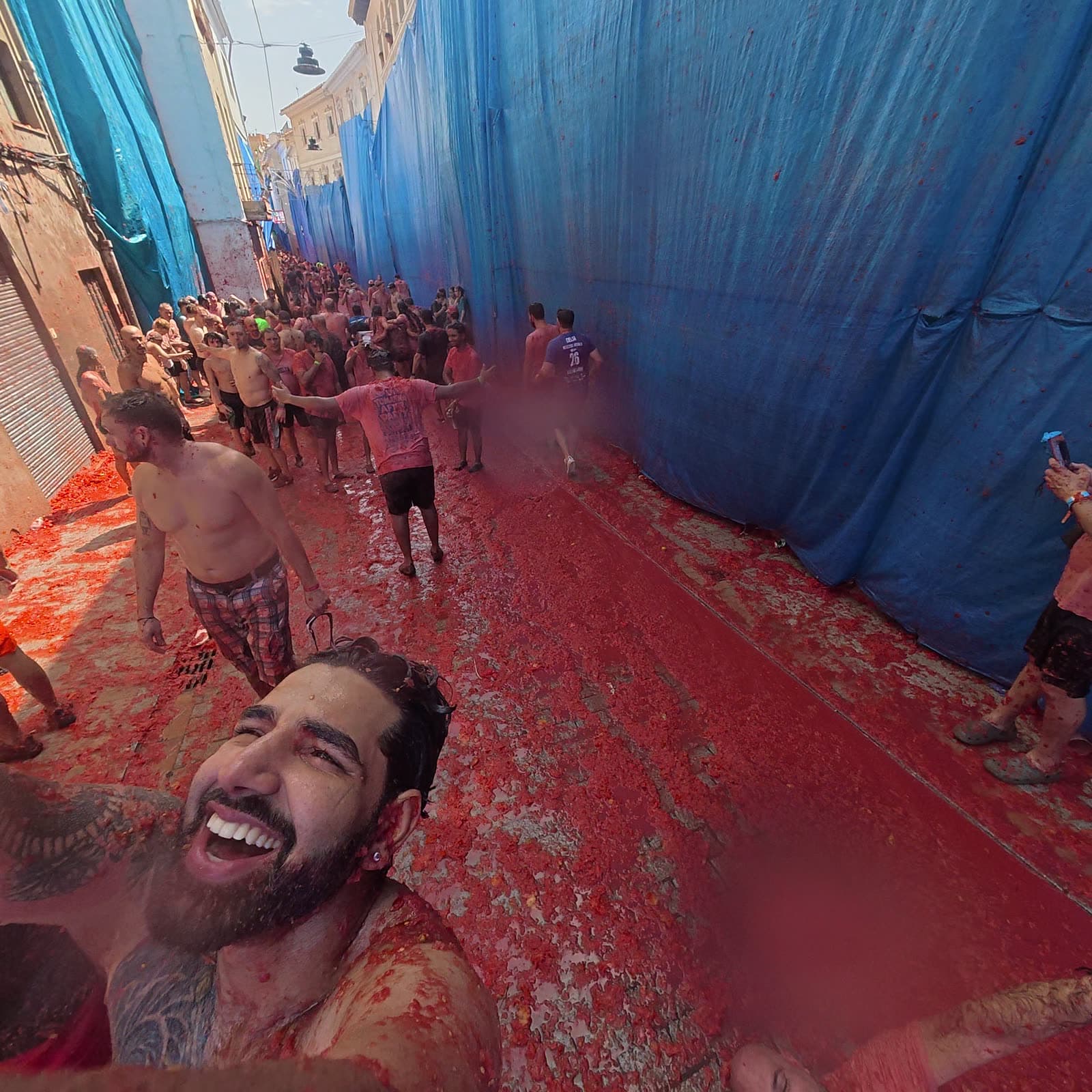 Me laughing in the foreground of a narrow street running red with tomato, the crowd walking out